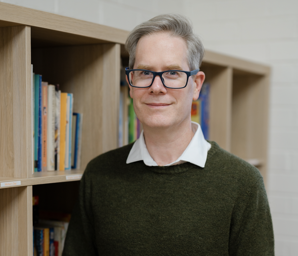 David Kinnane | Banter Speech & Language Man with glasses standing in front of a bookcase